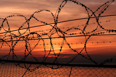 Silhouette barbed wire fence against sky during sunset