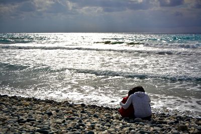 Rear view of woman with child on shore at beach against sky