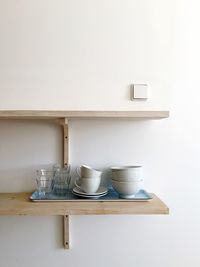 Cups and glasses with bowls on shelf against white wall