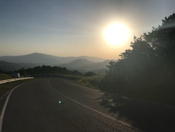 Road by mountains against sky during sunset