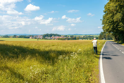 Rear view of person on road amidst field against sky