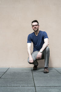 Young man crouching against wall