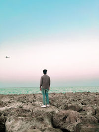 Rear view of man standing at beach against clear sky