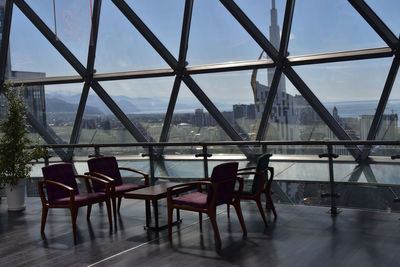 Chairs and tables in restaurant against sky seen through glass window