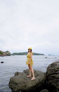 Full length of woman standing on rock by sea against sky