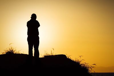 Low angle view of silhouette man standing against orange sky