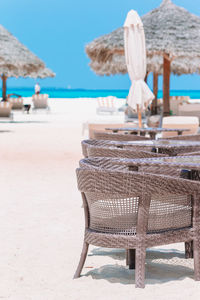 Empty chairs and table at beach against sky