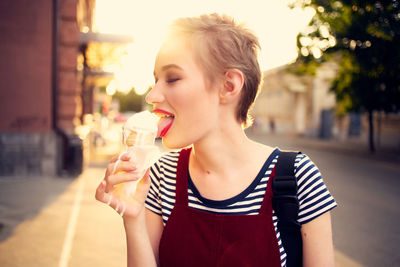 Portrait of young woman drinking ice cream in city