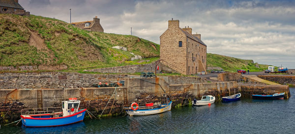 Sailboats moored on canal by buildings against sky