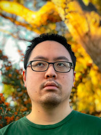 Portrait of young man wearing eyeglasses against trees and rowan berries during golden hour.