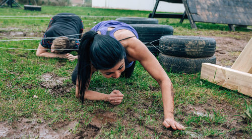 Woman crawling on grassy land under at boot camp