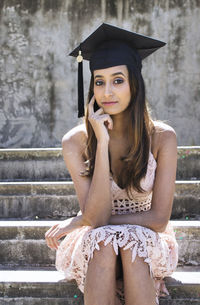 Portrait of young woman wearing mortarboard while sitting on steps