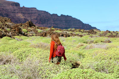 Woman with backpack standing amidst plants on land