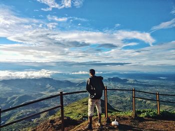 Man standing on railing against sea and mountains