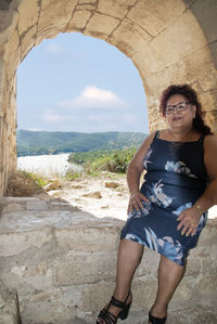 Woman sitting in archway against sea and sky