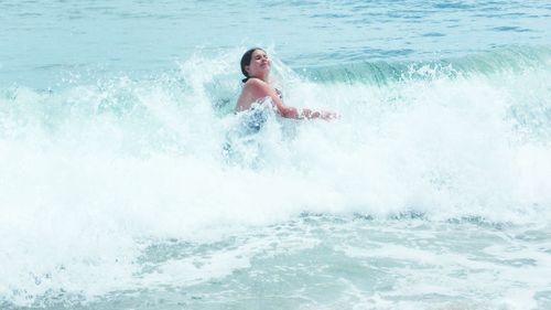 Full length of woman jumping in wave in sea