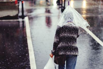 Rear view of person with umbrella walking on road during rainy season