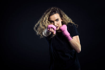 Portrait of female boxer standing against black background