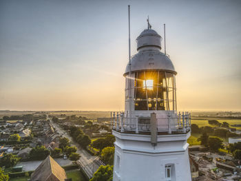 Lighthouse by building against sky during sunset