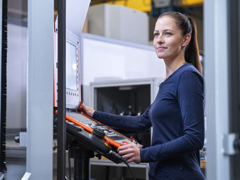 Smiling engineer standing near cnc machine panel at factory