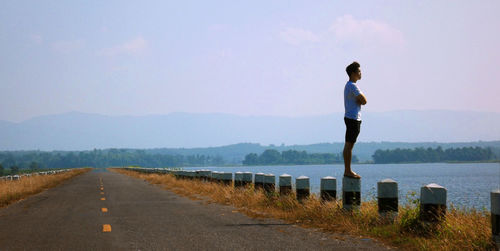 Man standing on bollard while looking at river