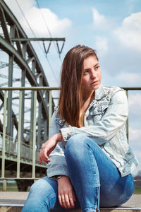 Beautiful young woman looking away while sitting against sky