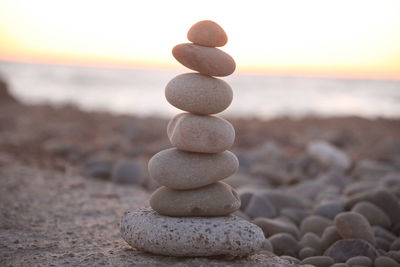 Stack of pebbles on beach against sky during sunset