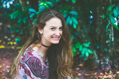 Portrait of smiling young woman standing against trees