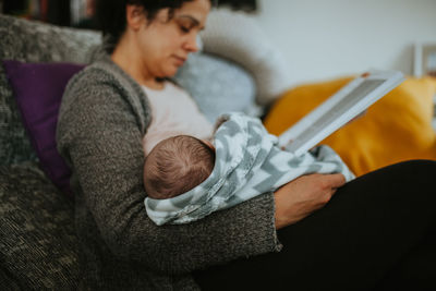 Mother holding baby while sitting on sofa at home