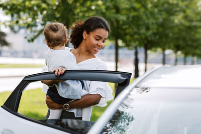 Mother holding baby standing by car outdoors