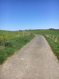 Dirt road amidst field against clear sky