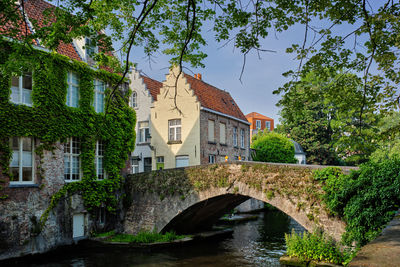 Arch bridge over river amidst buildings against sky