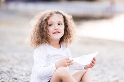 Girl looking away while holding paper boat at beach