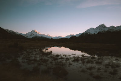 Scenic view of lake by mountains against sky during sunset