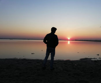 Silhouette man standing on beach against sky during sunset
