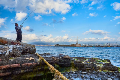 Man standing on rock by sea against sky