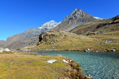 Lake in a valley in alpine national park in france with mountain peak background under blue sky