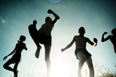 Low angle view of silhouette family jumping against sky during sunny day