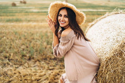 Smiling woman in sunglasses with bare shoulders on a background of wheat field and bales of hay.