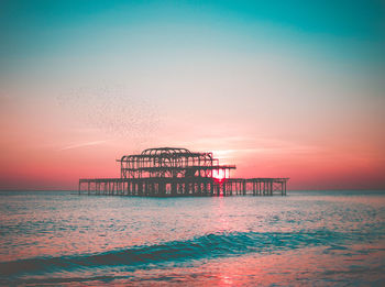 Silhouette cranes on beach against clear sky during sunset