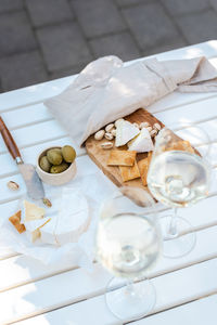 Wine appetizers namely pistachios, camembert cheese, saltine crackers, and olives on a white table.