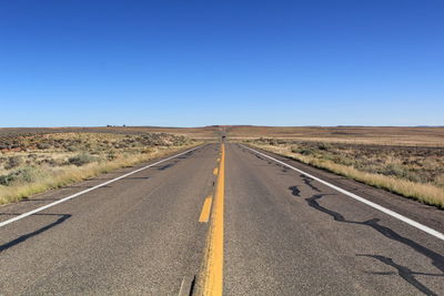 Empty long road amidst landscape against clear blue sky