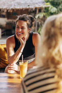 Smiling woman leaning on elbow while sitting with juice glass on table at wellness resort