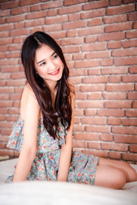 Portrait of a smiling young woman sitting against brick wall