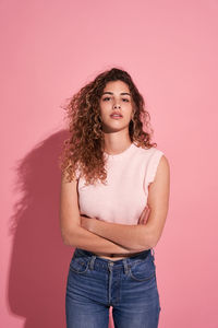 Portrait of a beautiful young woman standing against pink background