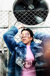 Smiling woman wearing sunglasses against chainlink fence during winter