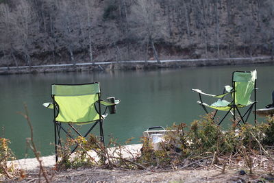 Chair on lakeshore against trees
