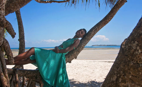 Portrait of young woman lying on branch at beach