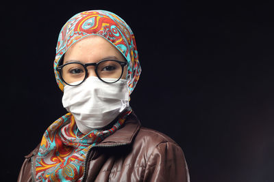 Portrait of woman in hijab standing against black background