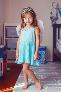 Portrait of a girl in fairy costume standing against wall on floor at home